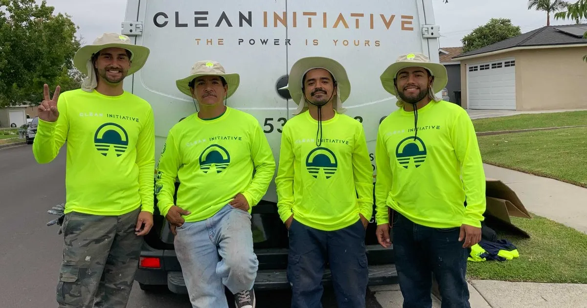 Four men in yellow Clean Initiative long-sleeved shirts stand in front of the rear of a van reading "Clean Initiative: The Power is Yours."